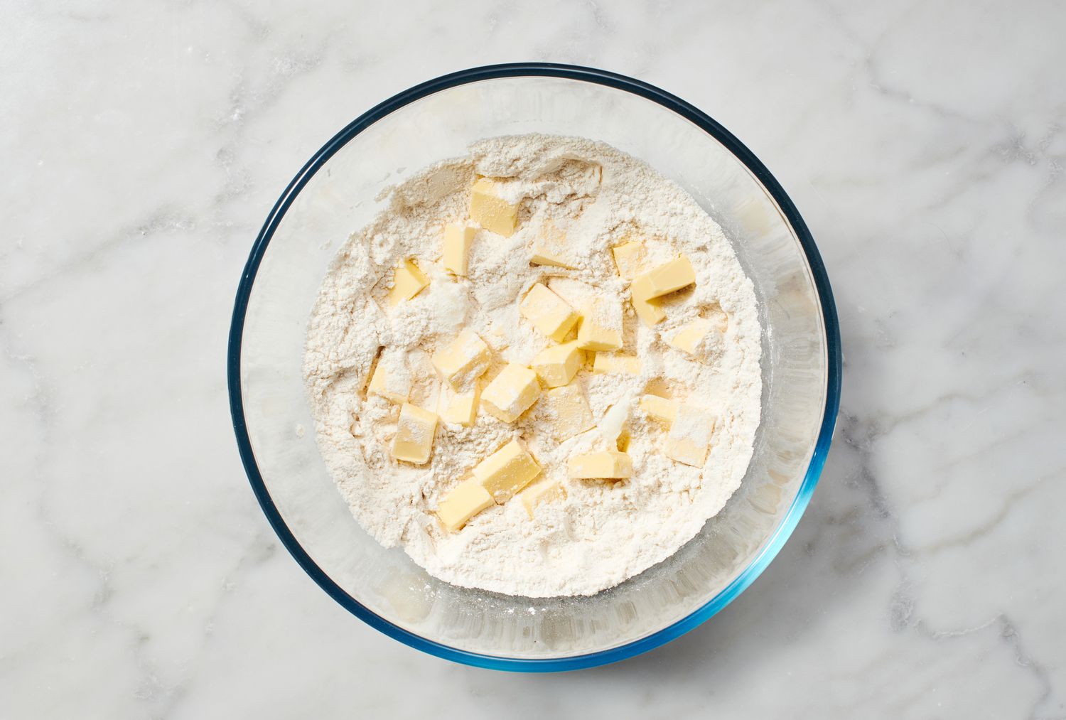 A bowl of flour and salt, with cubes of butter