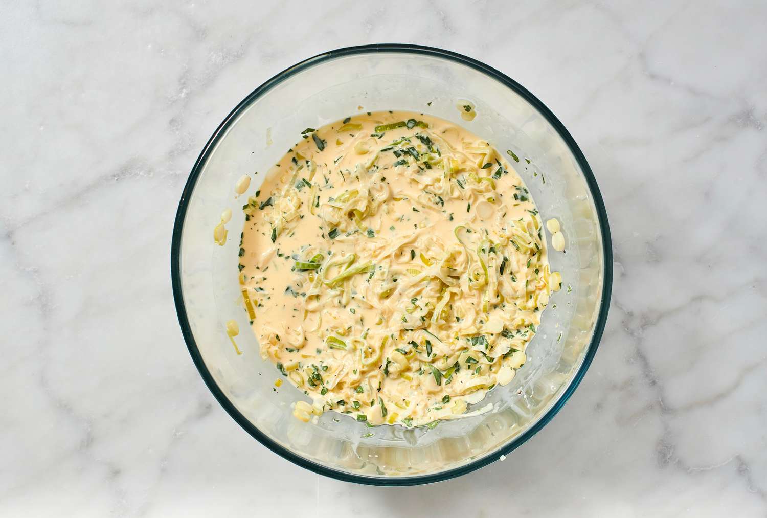 A bowl of whisked eggs, milk, heavy cream, lemon zest, salt, and pepper