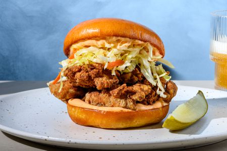 A crispy fried mushroom sandwich with cabbage slaw and mayo, served with a dill pickle spear and a glass of beer