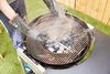 Hands holding grate above charcoals on the Weber Performer Deluxe