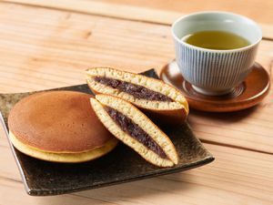 A plate with a pancake one full and the other is cut in half so you can see the inside. There is also a teacup place next to it full of tea and all of this is on a wooden table