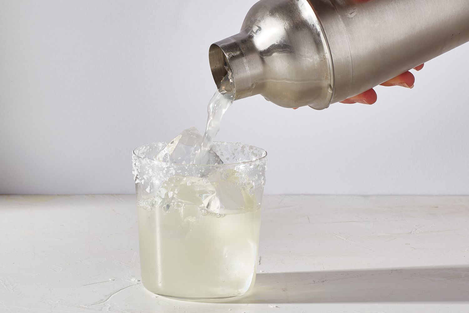 margarita being poured into prepared glass of ice from shaker