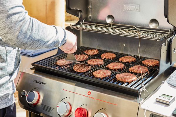 Person cooking burger patties on the Weber Genesis EX-325S Propane Gas Smart Grill