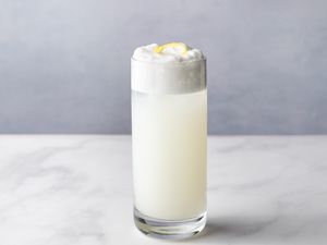 A gin fizz cocktail in a tall glass, garnished with a lemon peel