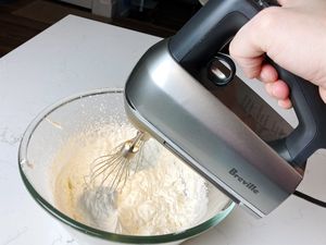 Person's hand holding the Breville The Handy Mix Scraper over a bowl of whipped cream