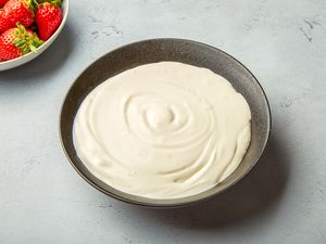 A bowl of homemade creme fraiche with strawberries in the background