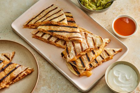 A platter of grilled honey chipotle chicken quesadillas, served with salsa, sour cream, and guacamole