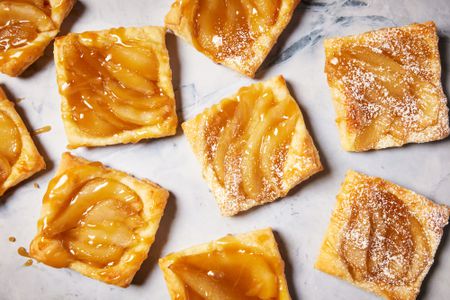 Individual pear tarts topped with powdered sugar and caramel on a marble surface