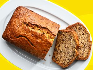 A loaf of banana bread on a white, oval platter with a couple slices cut