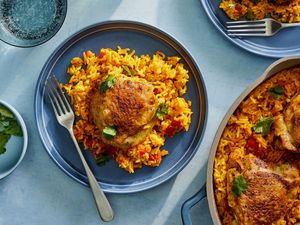 A serving of chicken thigh and tomato rice, next to a large pot of chicken and tomato rice