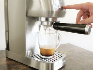 Hand pressing button on Casabrews 3700 Essential Espresso Machine dispensing espresso