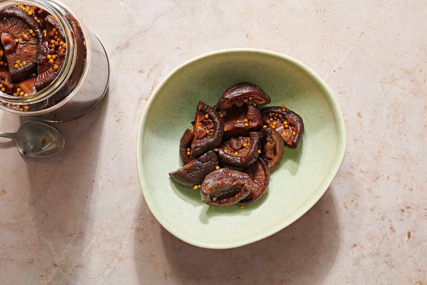 A bowl of soy sauce pickled shiitake mushrooms, next to a jar of pickled mushrooms