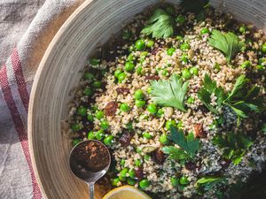 A bowl of quinoa and peas and parsley with a spoon showing a spoonful of the dish. The bowl is sitting on top of a napkin with two red stripes