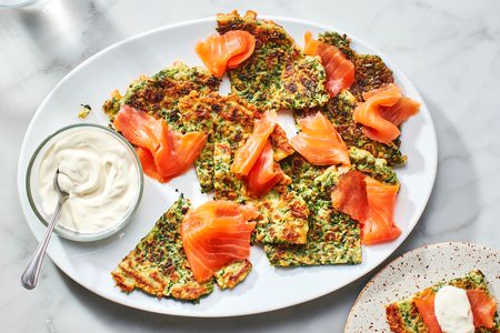 A platter of savory herb pancakes topped with lox, served with a small bowl of crème fraiche.