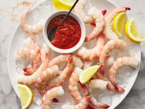 A large plate of shrimp cocktail, served on ice with lemon wedges and cocktail sauce