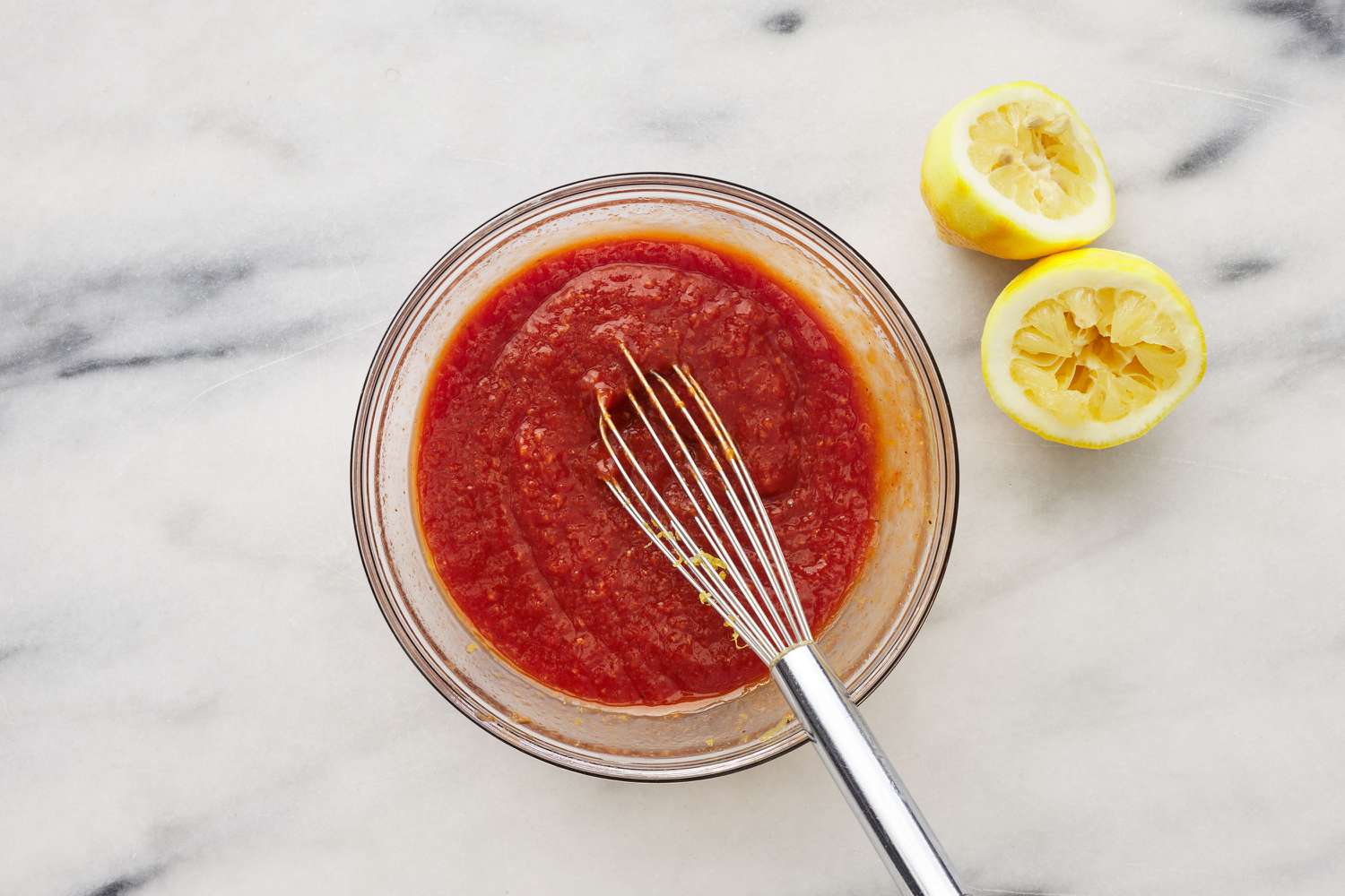 A small glass bowl of cocktail sauce, with a whisk stirring in lemon zest