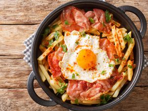 Pan full of thinly sliced potatoes that resemble fries that is topped with, garnish, seasoning, and a sunny side up egg