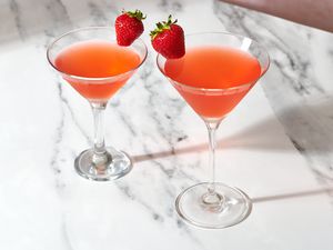 Two strawberry martinis on a marble surface, garnished with a fresh strawberry