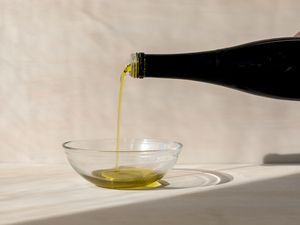 A hand pouring a bottle of olive oil into a small glass bowl