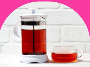 A French press filled with black tea, with a glass tea cup of tea