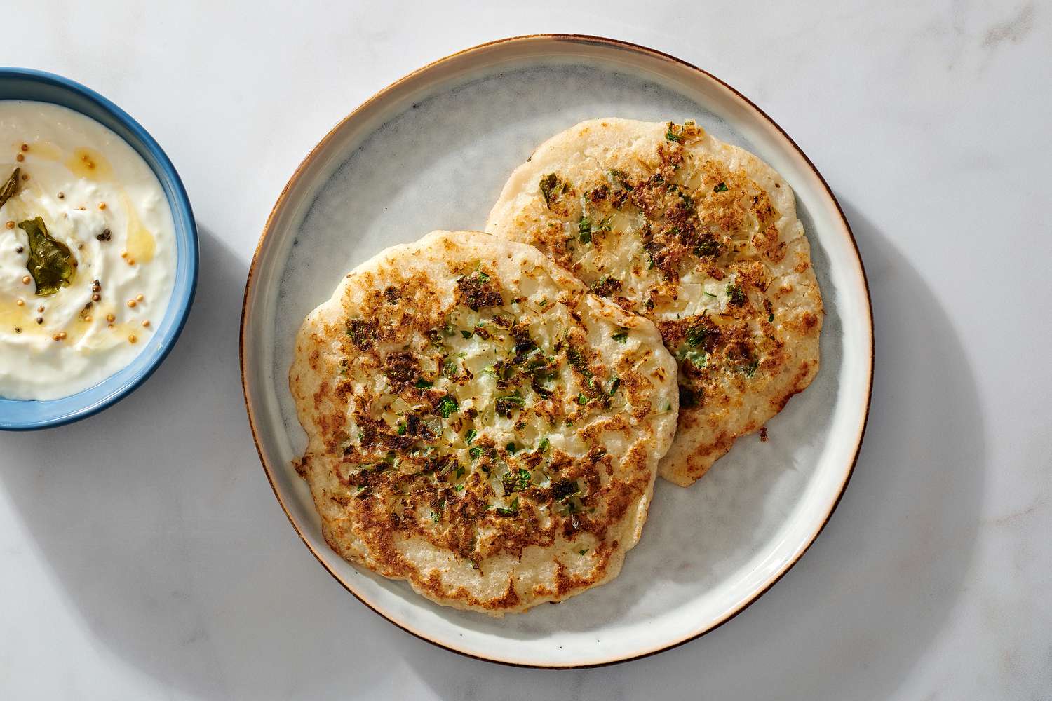 A plate with two uttapam, served with a small cup of yogurt dip