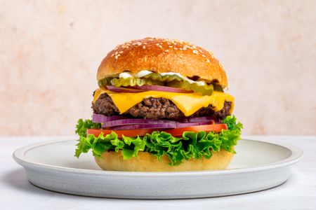 Burger with lettuce, tomato, onion, cheese, pickles, and mayo on a sesame bun