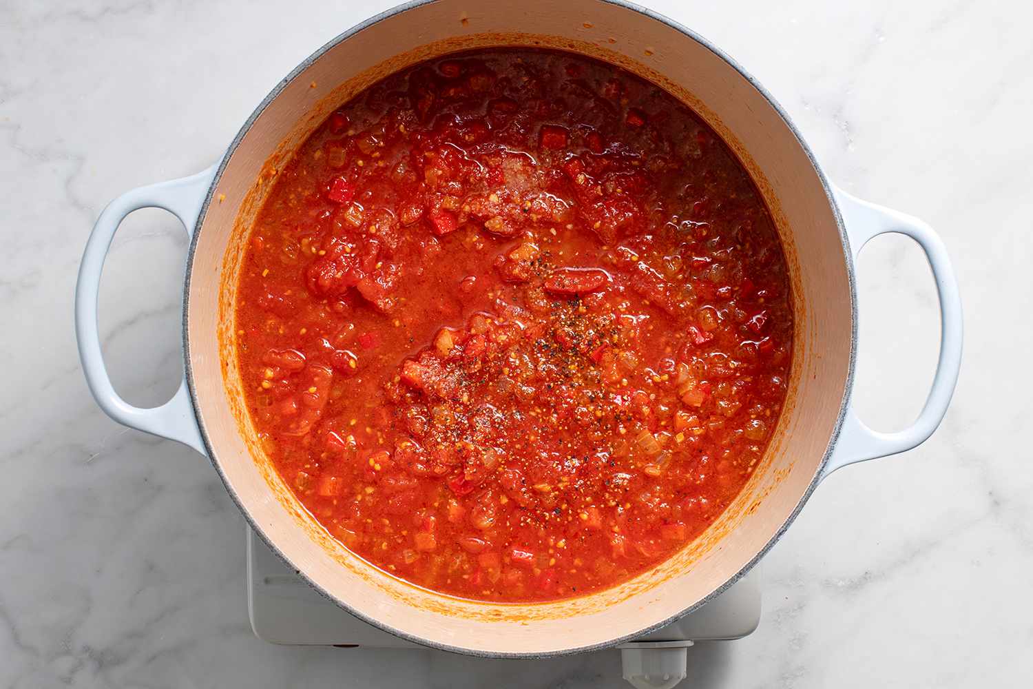 Tomatoes and their juice added to the spice mixture in the pot on a burner 