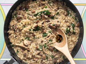 A pan filled with mushroom risotto and a wooden spoon with a whole in it. 