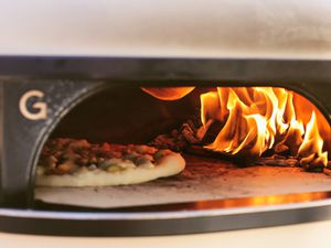 Pizza cooking next to a fire inside the Gozney Dome Pizza Oven