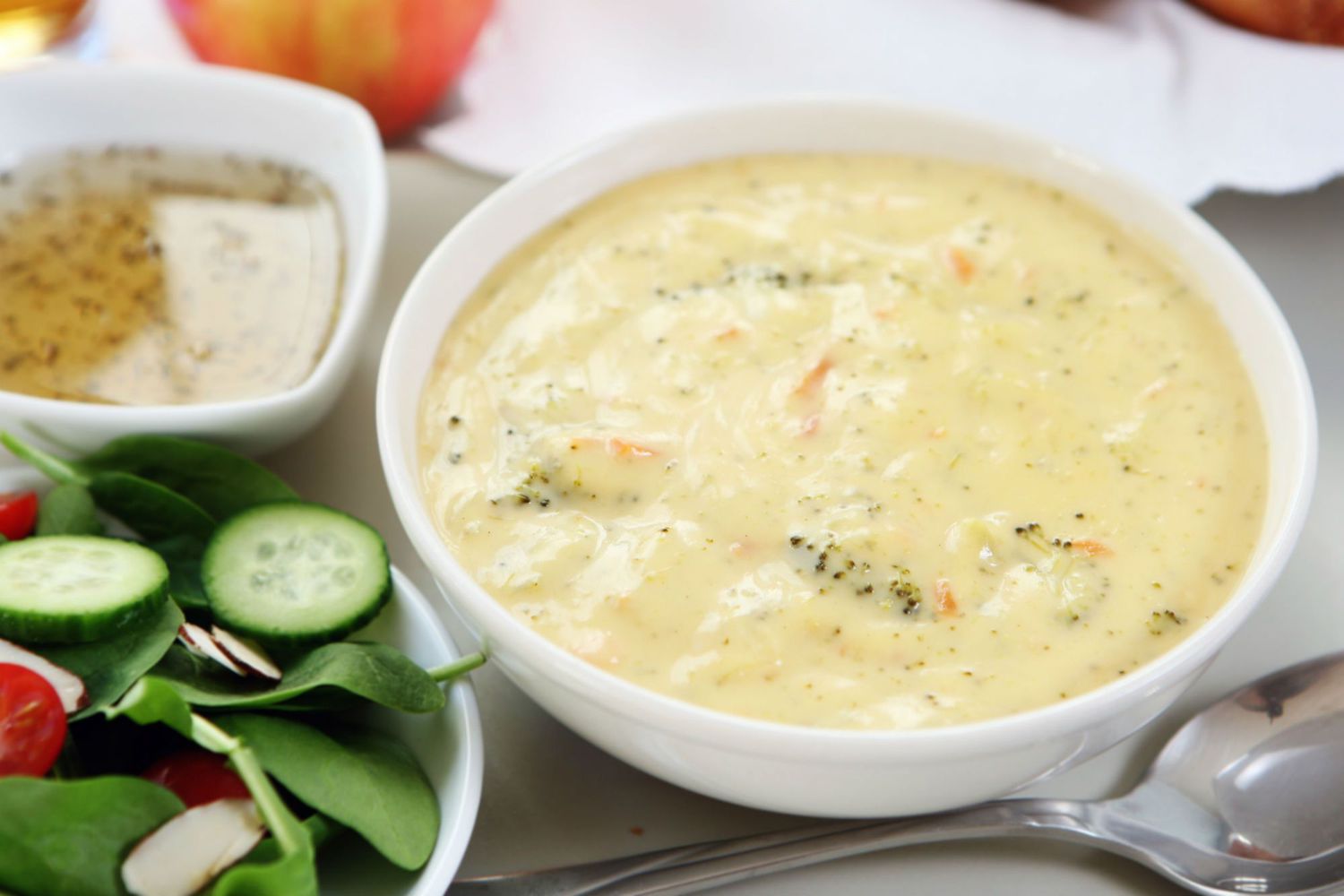 A bowl of broccoli and cheddar soup with a salad off to the side