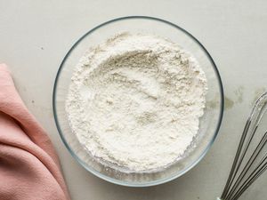 A clear bowl filled with flour next to a napkin and a whisk. 