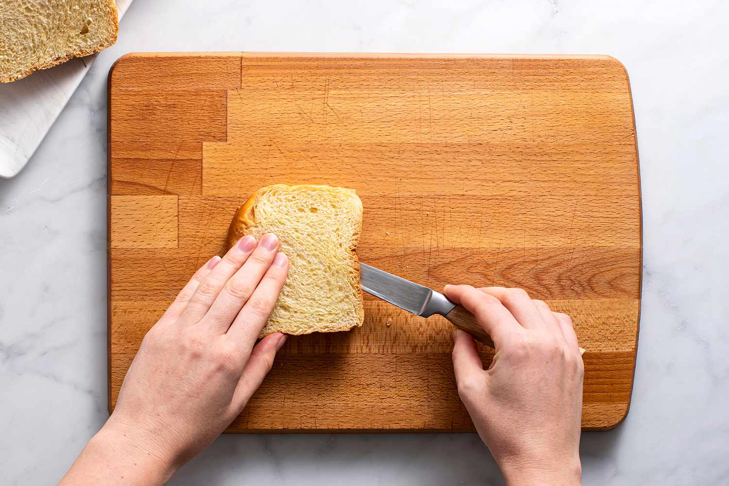 Slice of bread on cutting board with a pairing knife cutting into the side in order to create a cavity in the bread.