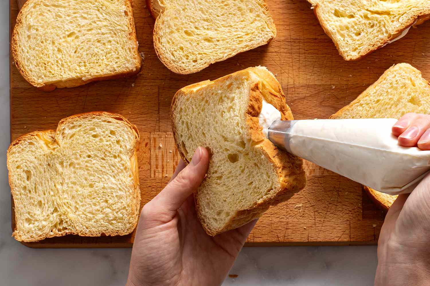 Slice of prepared bread being filled with cream cheese filling using a piping bag.