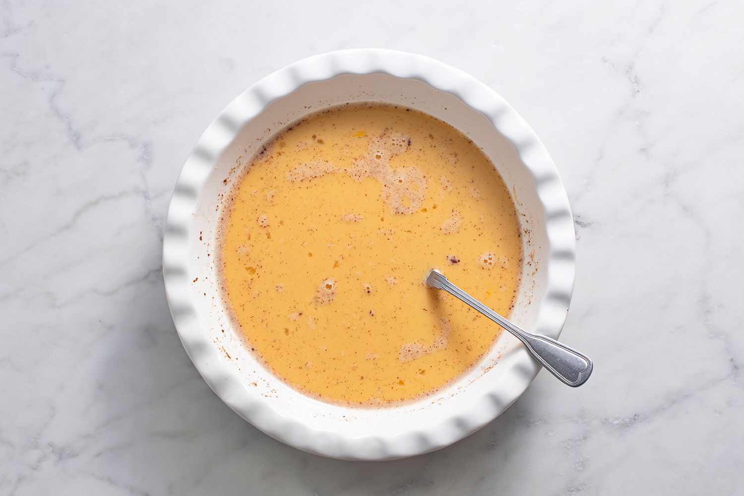 Eggs whisked with cinnamon and milk in a pie plate with a fork.