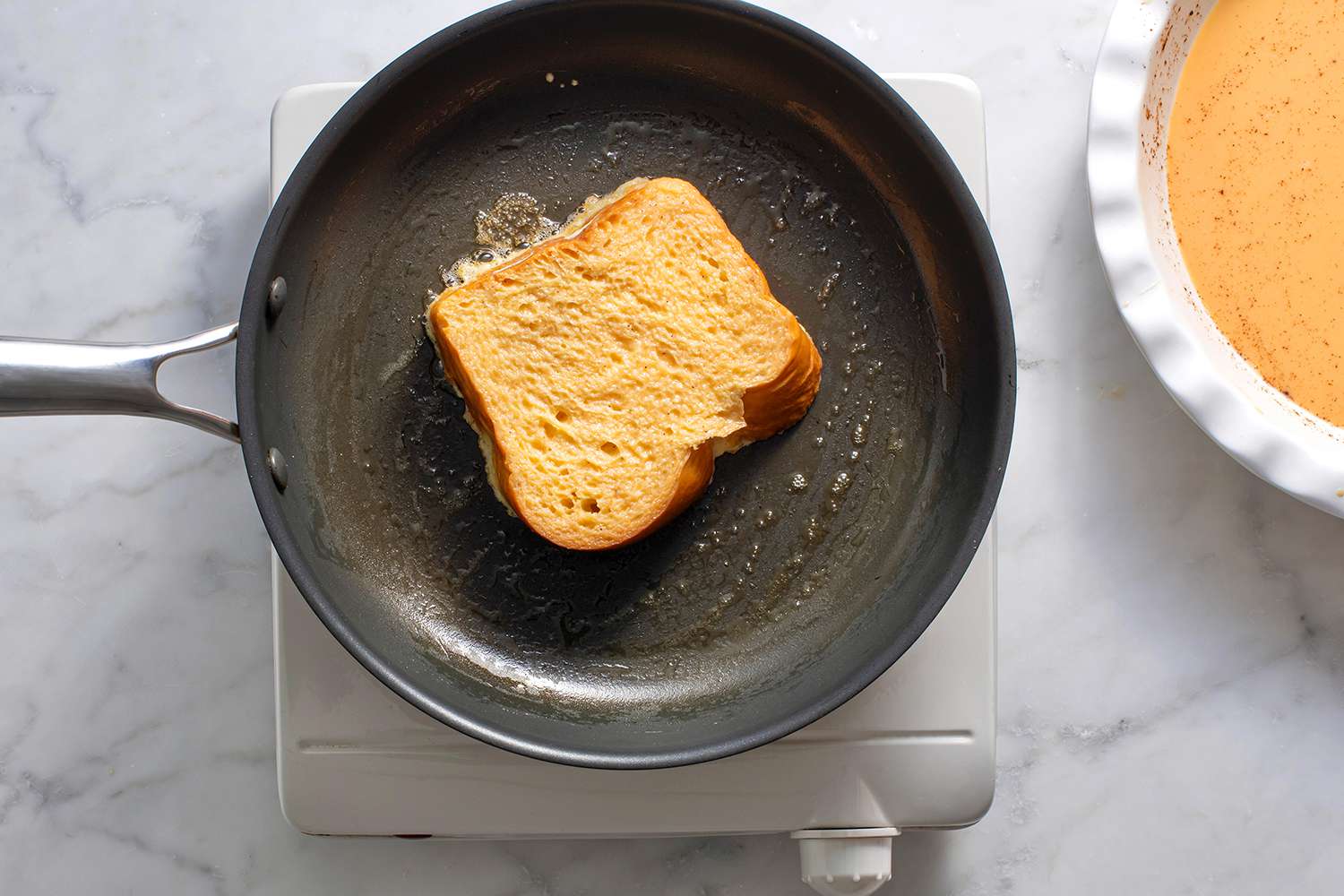 One piece of stuffed french toast in buttered skillet being cooked on one side.