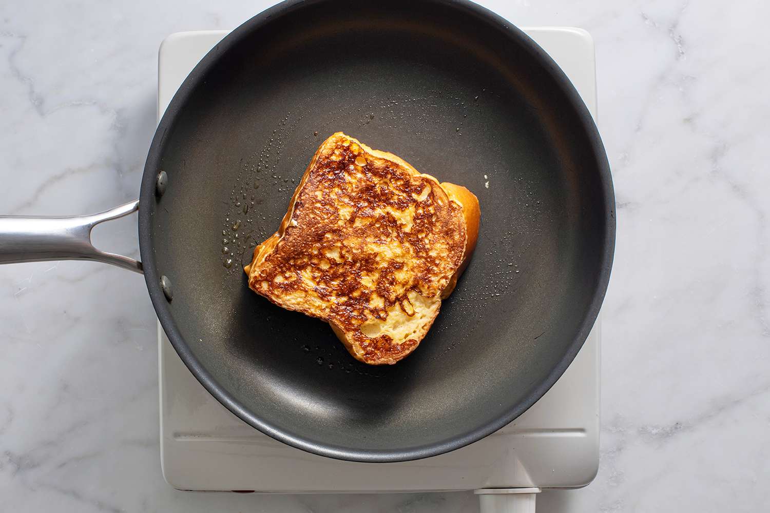 Stuffed french toast flipped onto other side for continued cooking, top of french toast is golden brown in color.