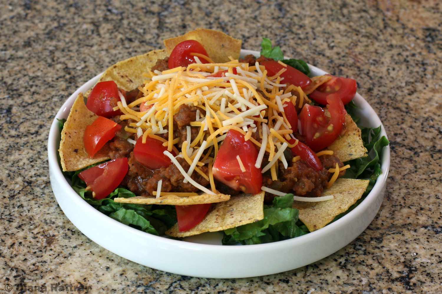 A taco salad covered in tortilla chips, cut tomatoes, and shredded cheese