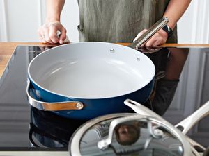 Person standing behind a Caraway Cookware Set saute pan displayed on glass stovetop