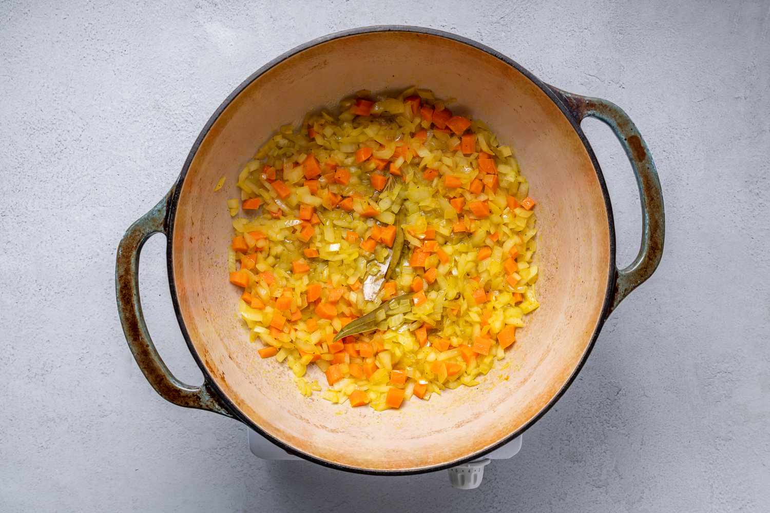 Carrots, onions, salt, turmeric, black pepper, and bay leaves cooking in a large pot