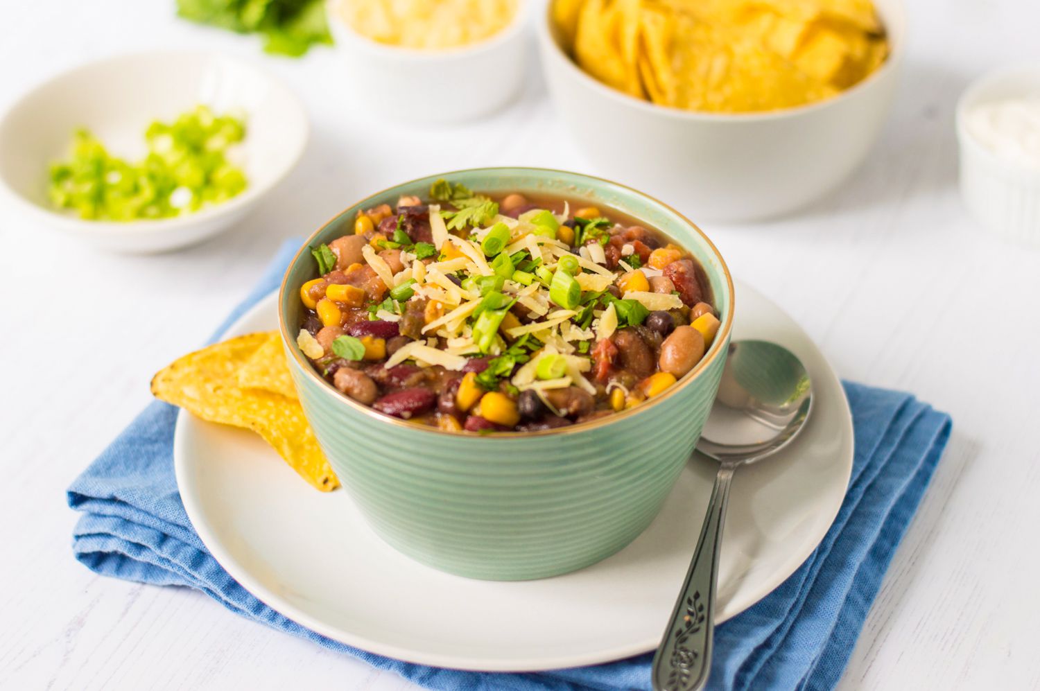 A light green bowl filled with vegetarian crock pot taco soup with a bowl of tortilla chips in the background