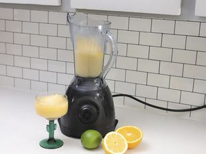 Vitamin One with a blended drink, a lime, and a sliced orange on a countertop