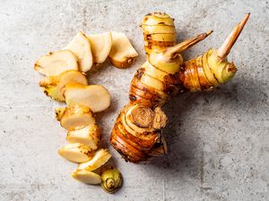 A whole Galangal and a slice one resting on a concrete surface 